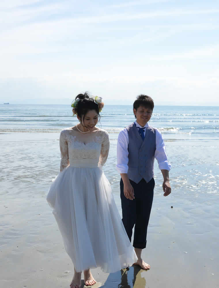 裸足で砂浜を歩く新郎新婦
